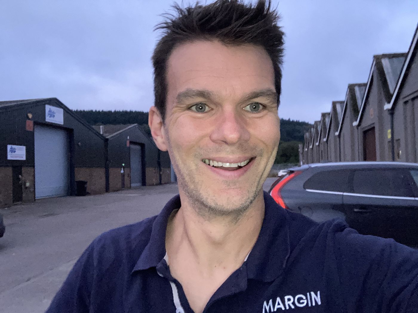 Ro grinning outside a factory unit in a navy MARGIN polo